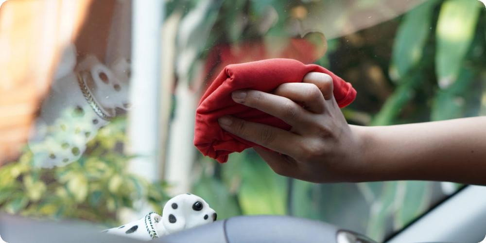 Eine Hand w&auml;scht mit einem roten Mikrofasertuch die Innenseite der Frontscheibe.