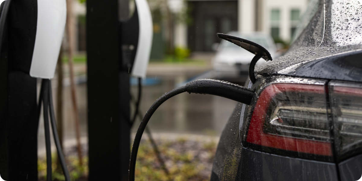 Elektroauto lädt an öffentlicher Ladestation im Regen, Nahaufnahme vom Ladeanschluss.