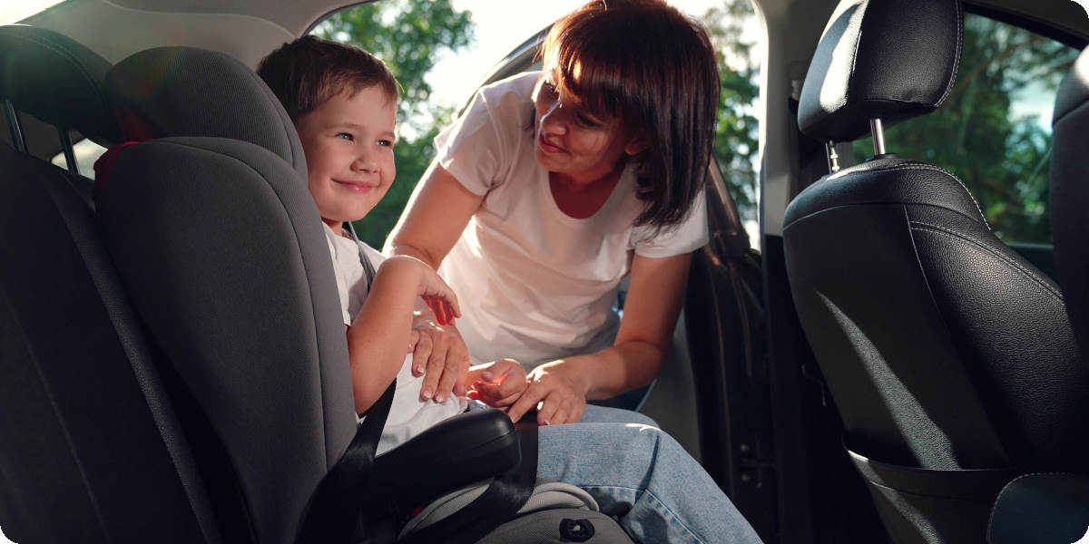 Frau schnallt Kind im Kindersitz auf dem R&uuml;cksitz eines Autos an.